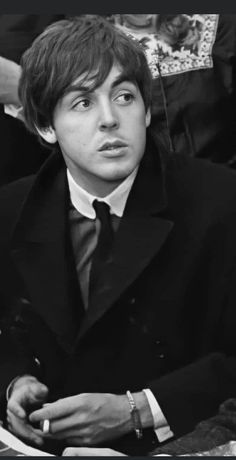 black and white photograph of young man in suit sitting at table with other people behind him