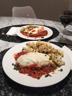 two white plates topped with food next to a glass of wine