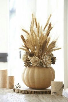 a white pumpkin decorated with dried flowers and feathers sits on a table next to a cork board