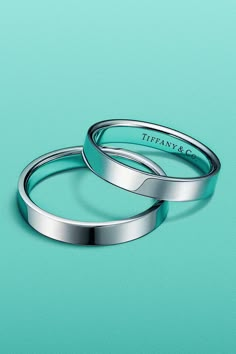 two silver wedding bands sitting on top of a blue surface with the words tiffany & co written on them