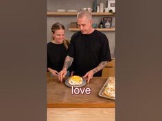 a man and woman standing in front of a table with food on top of it