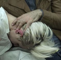 a woman with blonde hair laying on top of a man's stomach and sticking out her tongue