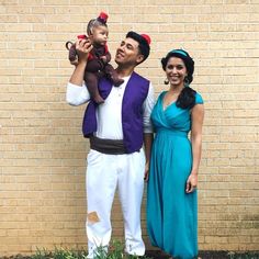 a man and woman are standing in front of a brick wall with a baby on his shoulders