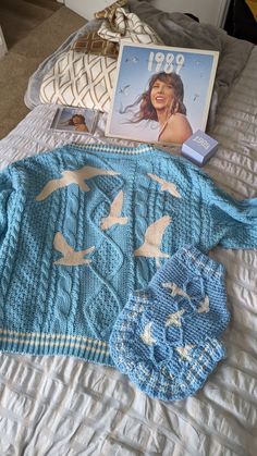 a knitted blue sweater with birds on it next to a magazine and some pillows