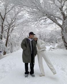 a man and woman standing in the snow next to trees with no leaves on them