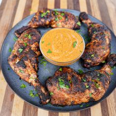 grilled chicken wings with dipping sauce on a black plate and wooden table top, ready to be eaten