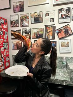 a woman eating a slice of pizza in front of a wall with pictures on it