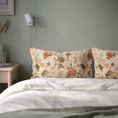 a bed with two pillows on top of it next to a night stand and lamp