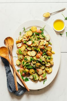 a white plate topped with potatoes and green beans next to two wooden spoons on a table