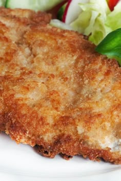 a white plate topped with fried chicken next to a salad and lettuce on top of it