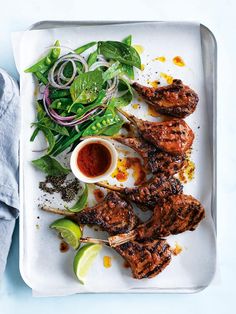 grilled meat and vegetables on a platter with dipping sauces, garnished with herbs