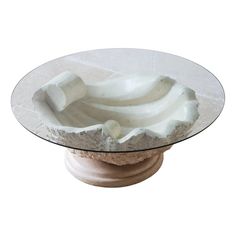 a glass table topped with white sculptures on top of a stone base and a circular glass plate