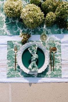 a place setting with napkins, silverware and green flowers on the tablecloth