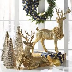 christmas decorations with deer, pine trees and wreath on window sill in white room