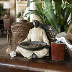 a statue sitting on top of a wooden table next to a basket and potted plant