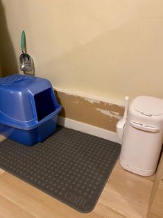 a blue litter box sitting on top of a wooden floor next to a trash can