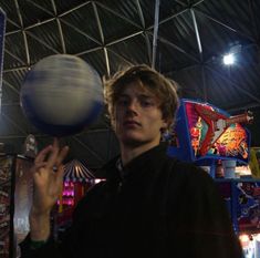 a young man is spinning a ball on his finger at an indoor game room with arcade machines