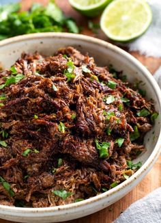 a bowl filled with shredded meat and garnished with cilantro, parsley and lime