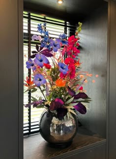 a vase filled with colorful flowers sitting on top of a wooden shelf