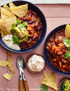 two bowls filled with chili and tortilla chips on top of a pink table