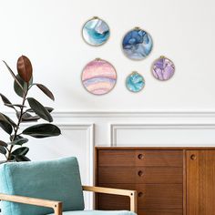 three circular paintings hang on the wall next to a blue chair and plant in a white room