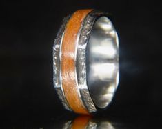 an orange and silver wedding ring with wood inlays on the inside, against a black background