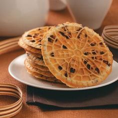 some cookies are on a white plate and brown table cloth next to two mugs