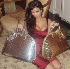 a woman in a red dress sitting on a chair holding two purses and one handbag