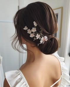 a woman with flowers in her hair is wearing a white dress and has one side bun up