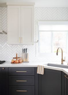 a kitchen with black cabinets and white tile backsplash, gold pulls on the faucet