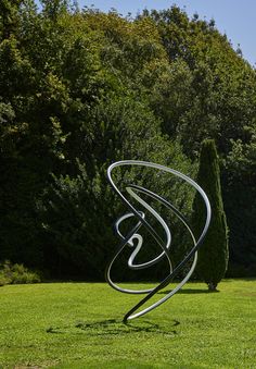 a metal sculpture in the middle of a grassy area with trees and bushes behind it