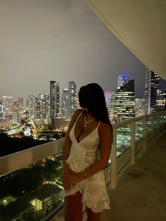 a woman standing on top of a balcony in front of a cityscape at night