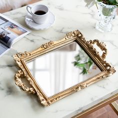 a mirror sitting on top of a table next to a cup of coffee and a magazine