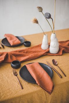 the table is set with black and white plates, silverware, and orange napkins