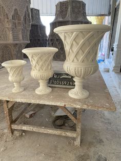 three white vases sitting on top of a table in front of some other statues