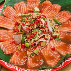 a red plate topped with lots of fish on top of a wooden table next to green leaves