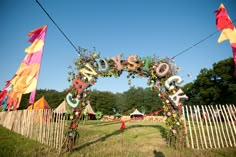 an archway decorated with letters and streamers in the middle of a grassy area next to a white picket fence