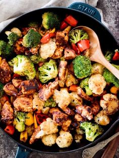 a skillet with broccoli, cauliflower and peppers in it next to a wooden spoon