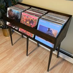 a wooden table topped with lots of records and a potted plant next to it