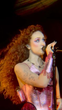 a woman with red hair holding a microphone in her right hand and wearing a corset