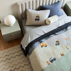 a bed with two pillows on top of it next to a night stand and lamp