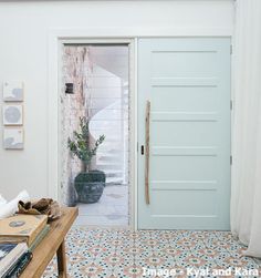 a room with a white door and blue tile floor next to a wooden coffee table