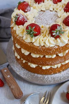 a cake with white frosting and strawberries is on a plate next to silverware