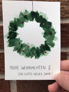 a hand holding up a card with a christmas wreath painted on it's front