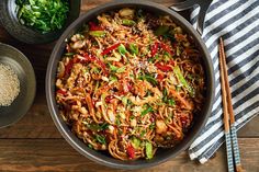 a pan filled with noodles and vegetables on top of a wooden table next to chopsticks