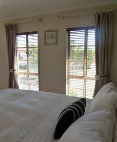 a large bed sitting in a bedroom next to two windows with blinds on each side