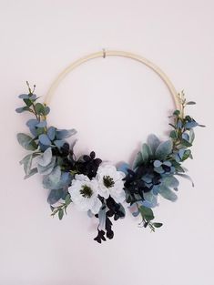 a wreath with white flowers and greenery hanging from it's side on a wall