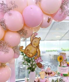 a table topped with lots of pink balloons and cake covered in frosting next to a window