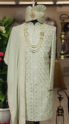 a mannequin wearing a white outfit with pearls on the neck and sleeves, standing next to a potted plant