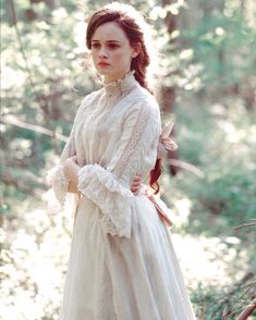 a woman in a white dress standing in the woods with her hands on her hips